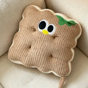 Svetlobraon kockasti Cuddle Puff jastuk sa talasastim ivicama, vezenim okicama i zelenim listićem, na krem fotelji