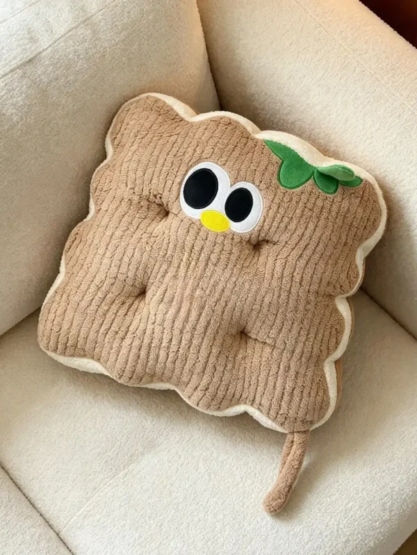 Svetlobraon kockasti Cuddle Puff jastuk sa talasastim ivicama, vezenim okicama i zelenim listićem, na krem fotelji