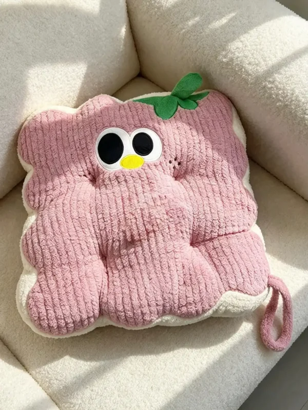 Roze kockasti Cuddle Puff jastuk sa talasastim ivicama, vezenim okicama i zelenim listićem, na krem fotelji