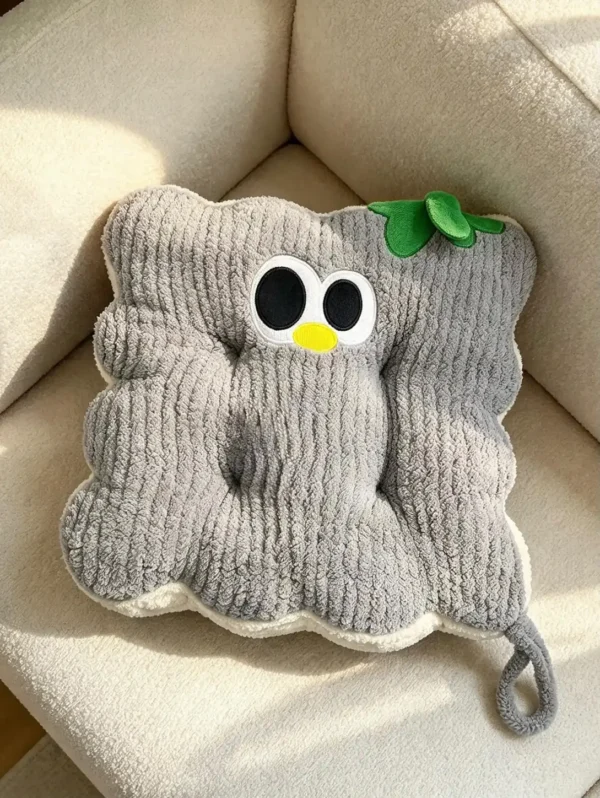 Sivi kockasti Cuddle Puff jastuk sa talasastim ivicama, vezenim okicama i zelenim listićem, na krem fotelji